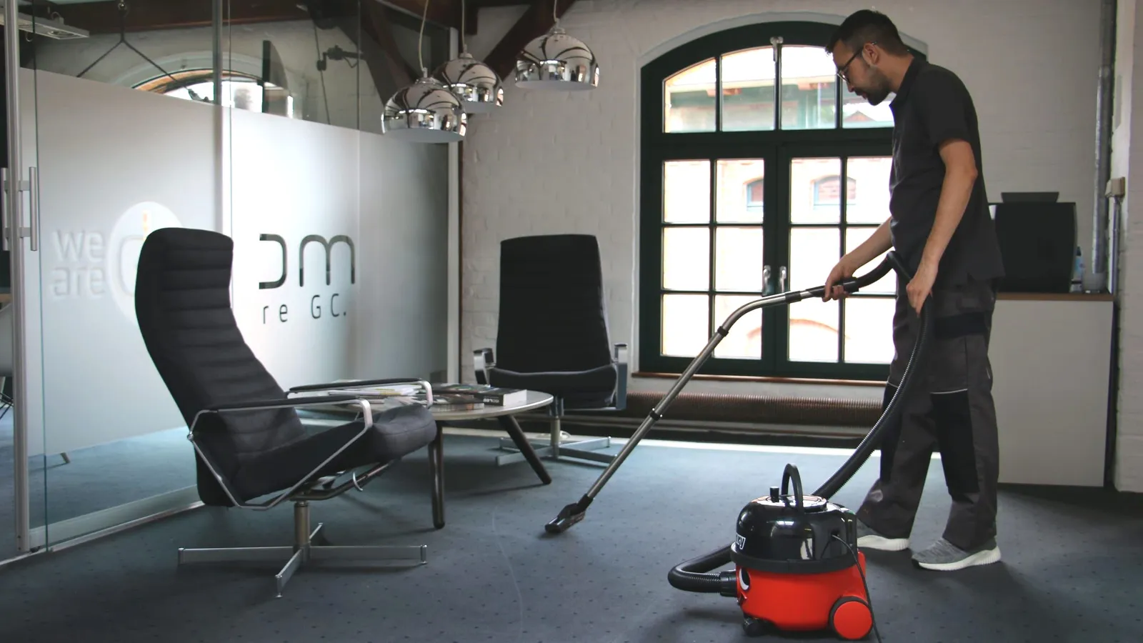 Büroreinigung: Mitarbeiter saugt den Teppichboden in einem Büro mit Besprechungsbereich
