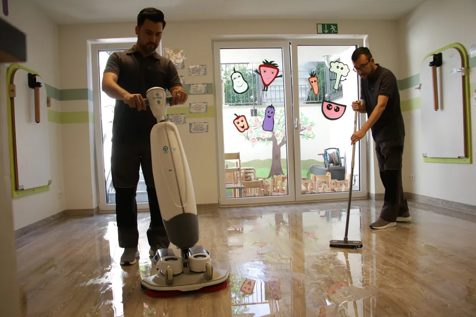 Zwei Barbat-Clean-Mitarbeiter reinigen den Boden einer Kita mit Maschine und Wischer